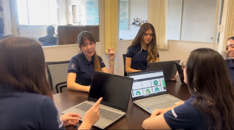 Membros da PCJ trabalhando em grupo ao redor de uma mesa, com notebooks abertos e um painel de gráficos na tela.